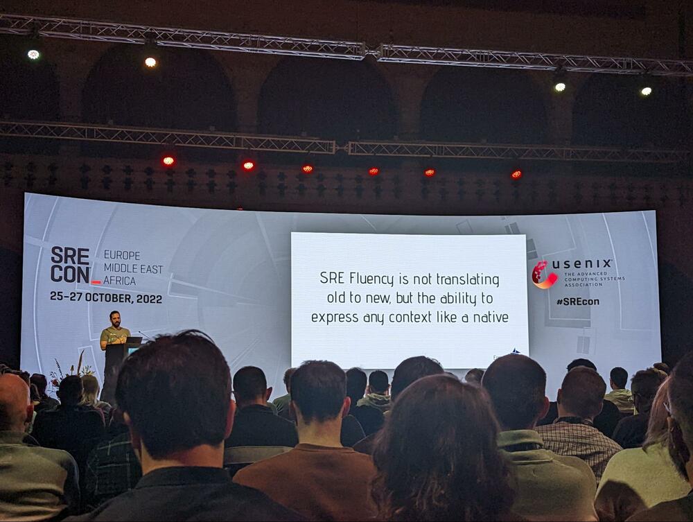 Andrew on stage with a slide saying &ldquo;SRE Fluency is not translating old to new but the ability to express any context like a native&rdquo;